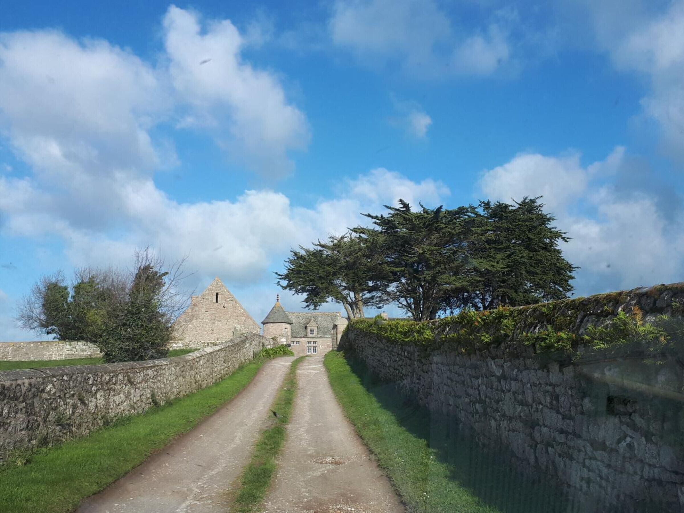 Ein Steinweg führt zu einem historischen Gebäude mit einem dreieckigen Dach und einem kleinen Turm.