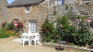 A stone house with a garden, white outdoor furniture, and blooming flowers.