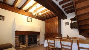 A cozy room with a fireplace, wooden beams, a dining table with chairs, and a television on the wall.