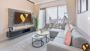 Egy modern nappali, melyben egy nagy televízió, egy kanapé, egy dohányasztal és egy balkon található, a balkonon pedig egy függőszék helyezkedik el.