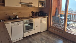 A compact kitchen with white cabinets, a dishwasher, an oven, and a microwave. There's a window to the right revealing a deck with outdoor furniture.