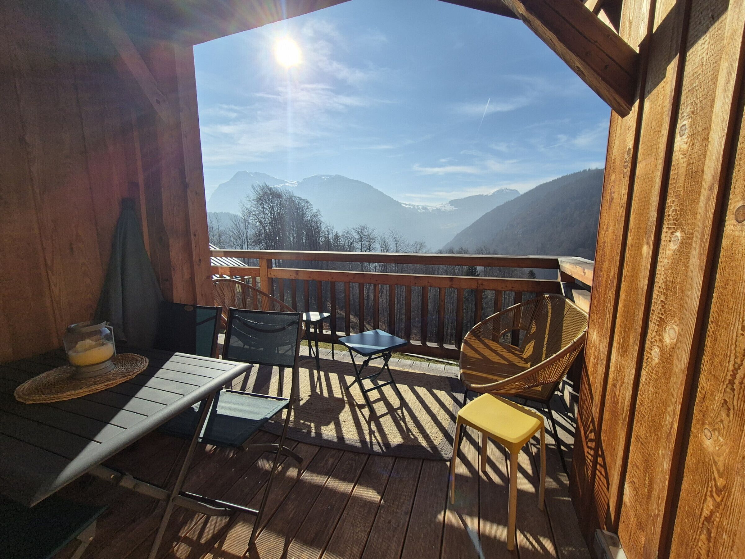 En træterrasse med et bord og stole, med udsigt over et bjergrigt landskab.