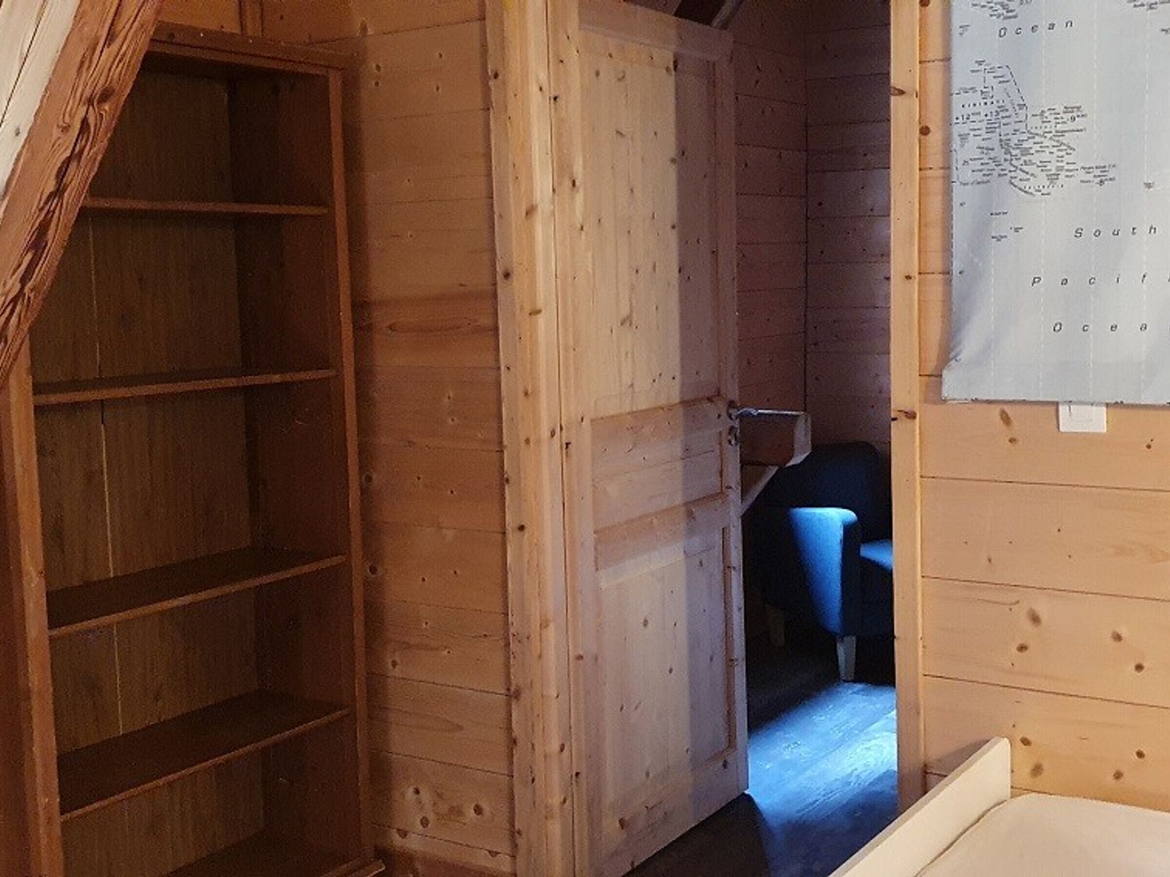 L’intérieur d’une cabane en bois, avec une grande étagère ouverte, une porte donnant sur une autre pièce et une carte accrochée au mur.