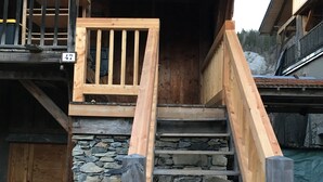 A wooden staircase with a stone wall base leading to a wooden deck.