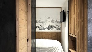 A narrow, wooden-framed room with a bed, a television mounted on the wall, and a mountain landscape mural.