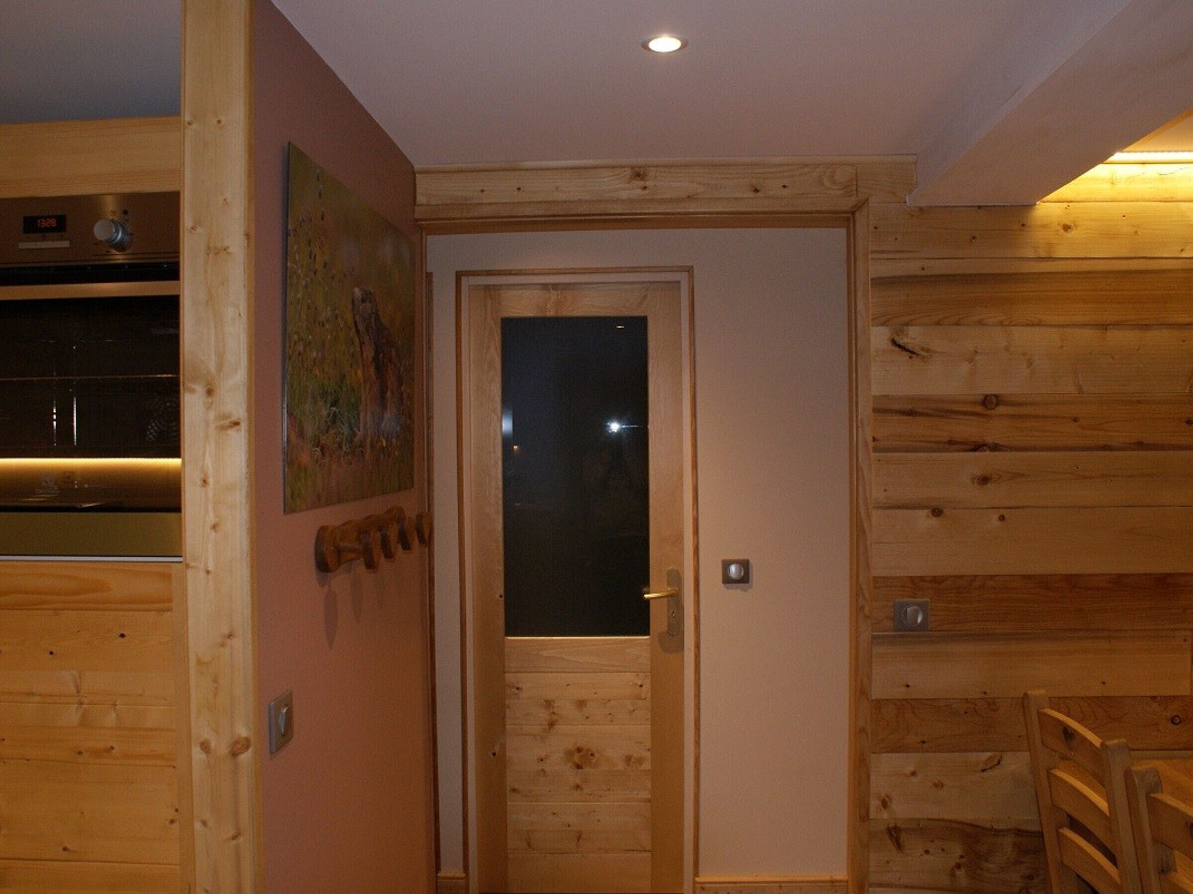 A wooden interior with a door, a wall-mounted light fixture, and a small table with chairs.