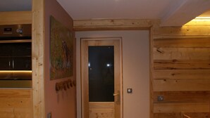A wooden interior with a door, a wall-mounted light fixture, and a small table with chairs. - Renovated 50 m² apartment, 2 bedrooms, central, WIFI (Les Carroz d'Arâches)