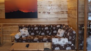A cozy cabin interior with a wooden wall, a large painting of a sunset, a patterned sofa, and a small wooden table. - Renovated 50 m² apartment, 2 bedrooms, central, WIFI (Les Carroz d'Arâches)