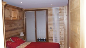 A bedroom with a wooden headboard, a bed with red bedding, a nightstand with a lamp, and a sliding glass door with a white radiator. - Renovated 50 m² apartment, 2 bedrooms, central, WIFI (Les Carroz d'Arâches)