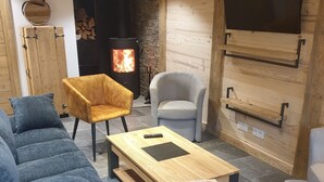 Un salon chaleureux avec un grand canapé, une table basse en bois et deux fauteuils. Une cheminée avec un feu visible apporte une touche de chaleur à l’espace.