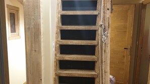 Un escalier étroit en bois mène au deuxième étage, avec une porte en haut et une petite fenêtre sur le côté gauche.