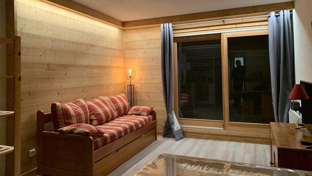 Ein gemütliches Zimmer mit Holzwand, einer Couch, einer Lampe und einer Schiebetür aus Glas.