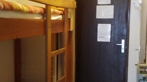 Ein Etagenbett mit gemustertem Bettbezug, eine dunkle Tür mit Papieren und ein Heizkörper.