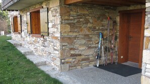 Ein Steinhaus mit Holztür und Fenstern, einer Steintreppe und Ski, die an der Wand lehnen.