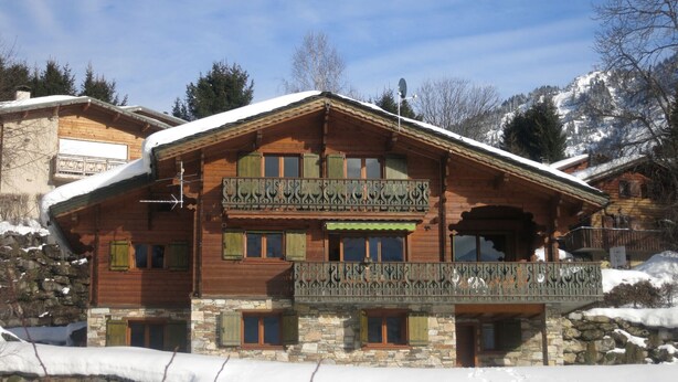 Eine Holzhütte mit Balkon und Steinfundament, umgeben von Schnee.