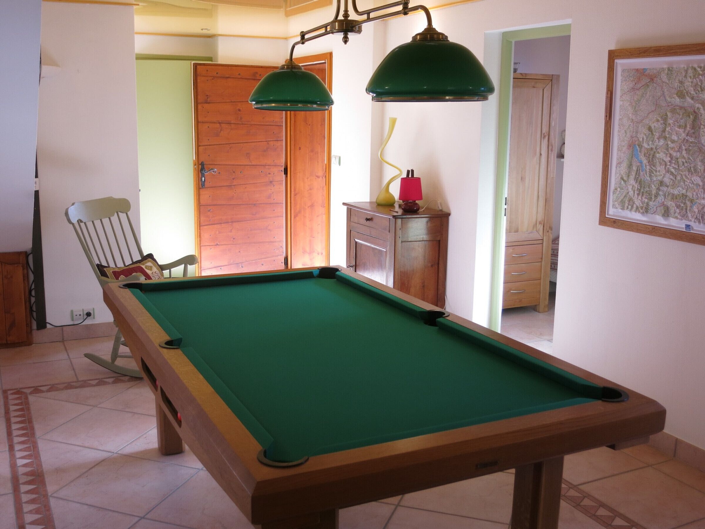 Una mesa de billar con superficie de fieltro verde, estructura de madera y dos lámparas verdes encima.