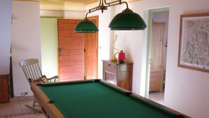 Ein Billardtisch mit grüner Spielvliesdecke, Holzrahmen und zwei grünen Lampen darüber.