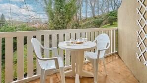 A balcony with white plastic chairs and a small round table, overlooking a garden with trees and a distant view. - Charming T2 in Barbotan: WIFI, Pets, Parking (Barbotan-les-Thermes)
