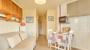 A compact living space with a sofa, a dining table set for two, and a kitchenette with a microwave. - Charming T2 in Barbotan: WIFI, Pets, Parking (Barbotan-les-Thermes)