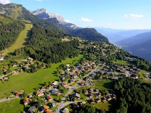 An aerial view of a village with houses, roads, and mountains in the background.