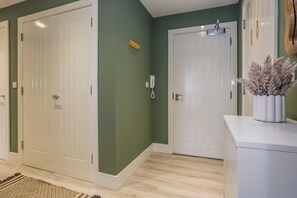 A hallway with two white doors, a phone on the wall, and a decorative plant on a white console table.