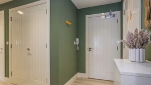 A hallway with two white doors, a phone on the wall, and a decorative plant on a white console table. - The Sapphire at Parsons House (Washington)