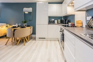 A modern kitchen with white cabinets, a dining area with a round table, and a light-colored floor.