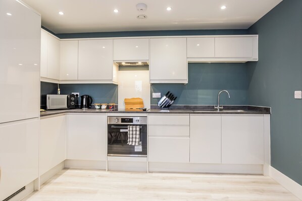 A compact kitchen with white cabinets, a built-in oven, a microwave, and a sink.