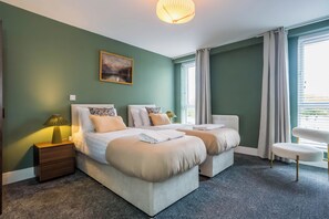 Ein modernes Hotelzimmer mit zwei Betten, einem Nachttisch mit Lampe, einem Sessel und einem Bild an der Wand.
