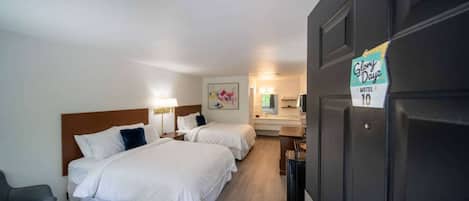 Habitación de motel con dos camas, un escritorio, una silla y la puerta del baño.