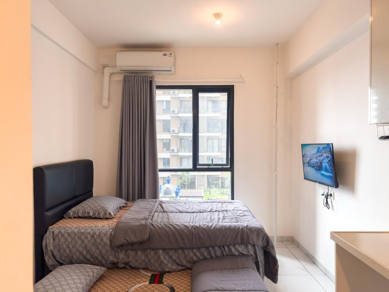A bedroom with a bed, a TV, and a window with a view of buildings.