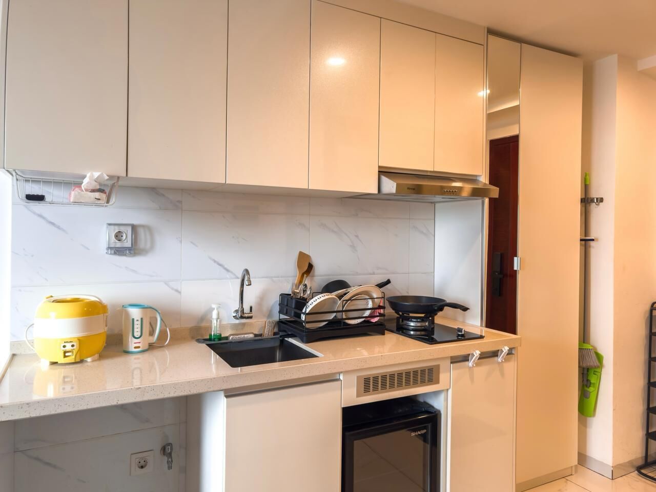 Une cuisine moderne avec des armoires blanches, une hotte de cuisinière en acier inoxydable, un lave-vaisselle encastré et un plan de travail sur lequel se trouvent un appareil jaune et une bouilloire.
