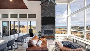 Amplia sala de estar con chimenea de piedra, sofás de cuero, una mesa de comedor y grandes ventanales con vista al paisaje.