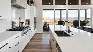 Una cocina moderna con armarios blancos, una isla grande con fregadero y vistas a un paisaje pintoresco a través de amplios ventanales.