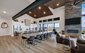 A modern kitchen with a long island, black bar stools, and a stone fireplace.