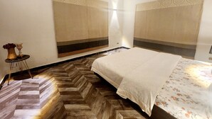 A hotel room with a bed, a small table with a vase, patterned curtains, and a herringbone floor.