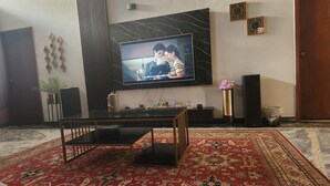 A living room with a TV mounted on a marble wall, a dining table, and a patterned carpet.