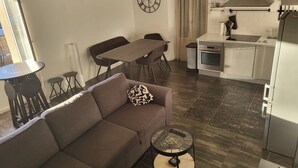 Ein modernes Wohnzimmer mit Sofa, Esstisch und Küchenzeile, inklusive Herd und Schränken.