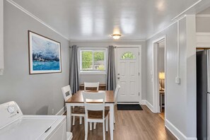 Un área de comedor con una mesa y sillas, una ventana con cortinas, una puerta y una lavadora.