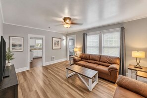 Una sala moderna con un sofá de cuero marrón, una mesa de centro de madera y un ventilador de techo.