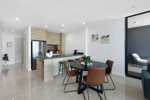 Una cocina moderna con una isla central, una zona de comedor con una mesa redonda y sillas, y un ventanal que da a un balcón.