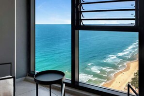 A room with a large window overlooking a beach and ocean.