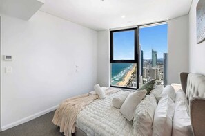 A bedroom with a large window overlooking a cityscape and beach.