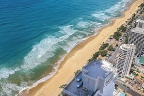 Un hotel frente al mar, con vista a la playa, junto a una orilla arenosa y el océano.