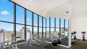 Een sportschool met diverse trainingsapparaten, grote ramen en uitzicht op een stadsgezicht.