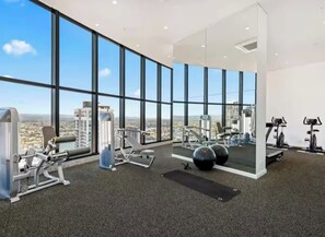 A gym with various exercise equipment, large windows, and a view of a cityscape.
