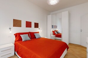 A bedroom with a large bed, white wardrobe, and a mirror.