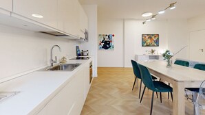 Una cocina moderna con armarios blancos, un lavamanos de acero inoxidable y una zona de comedor con una mesa de madera y sillas color turquesa.