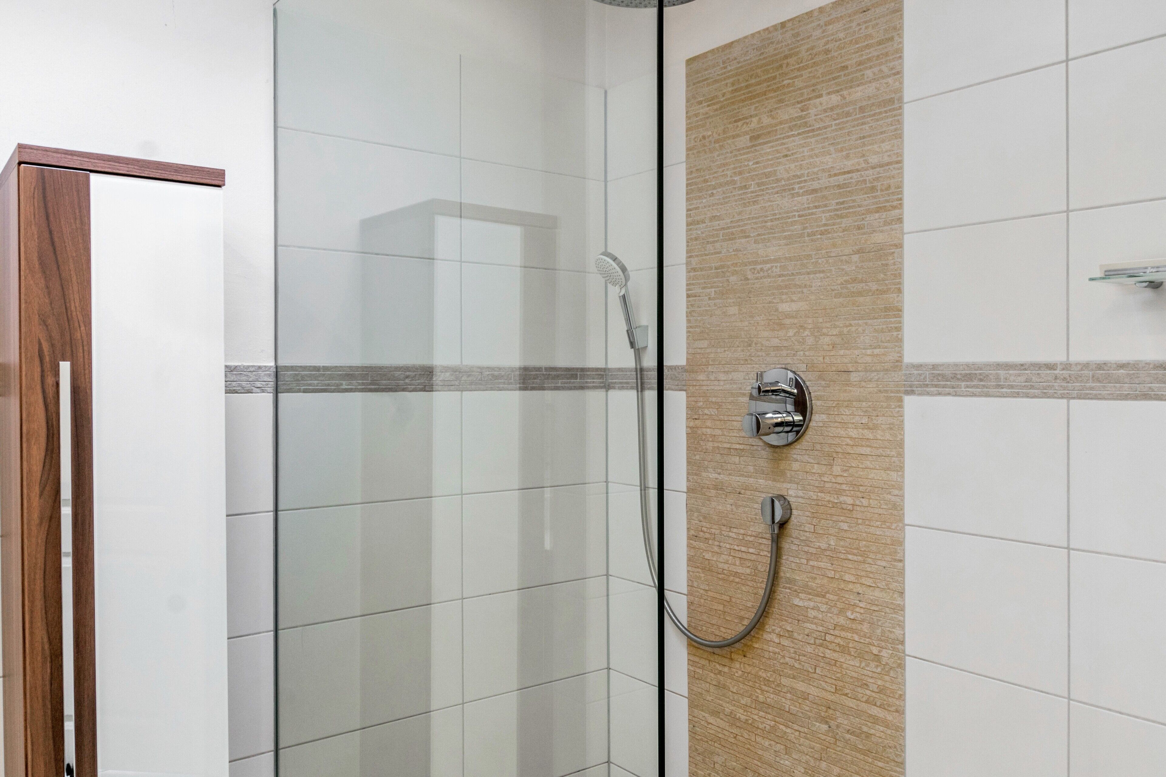 Ducha con cerramiento de vidrio, cabezal de ducha manual y llave en la pared.