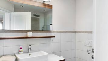 Une salle de bain avec un lavabo blanc, un miroir et une douche.